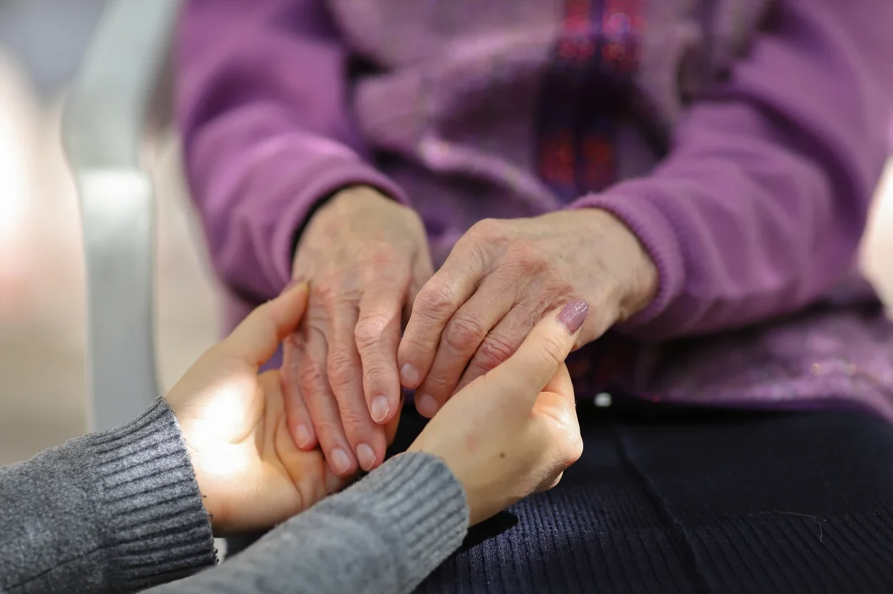 Caregiver gently holding the hands of a senior resident